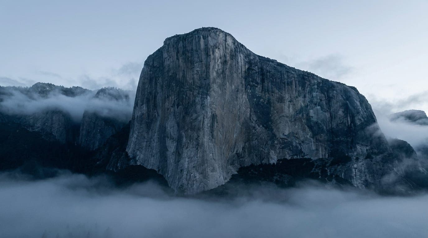 Kühle Alpenlandschaft in Blaustunden-Tönen: ein massiver, fest stehender Granitgipfel über treibendem Nebel.