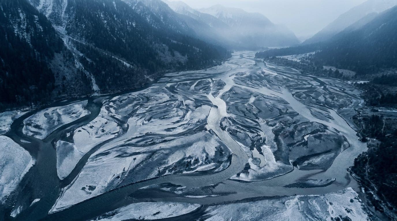 Kühle Alpenlandschaft in Blaustunden-Tönen: ein weitläufiges Flussdelta, dessen silberne Arme sich aus der Vogelperspektive auffächern.