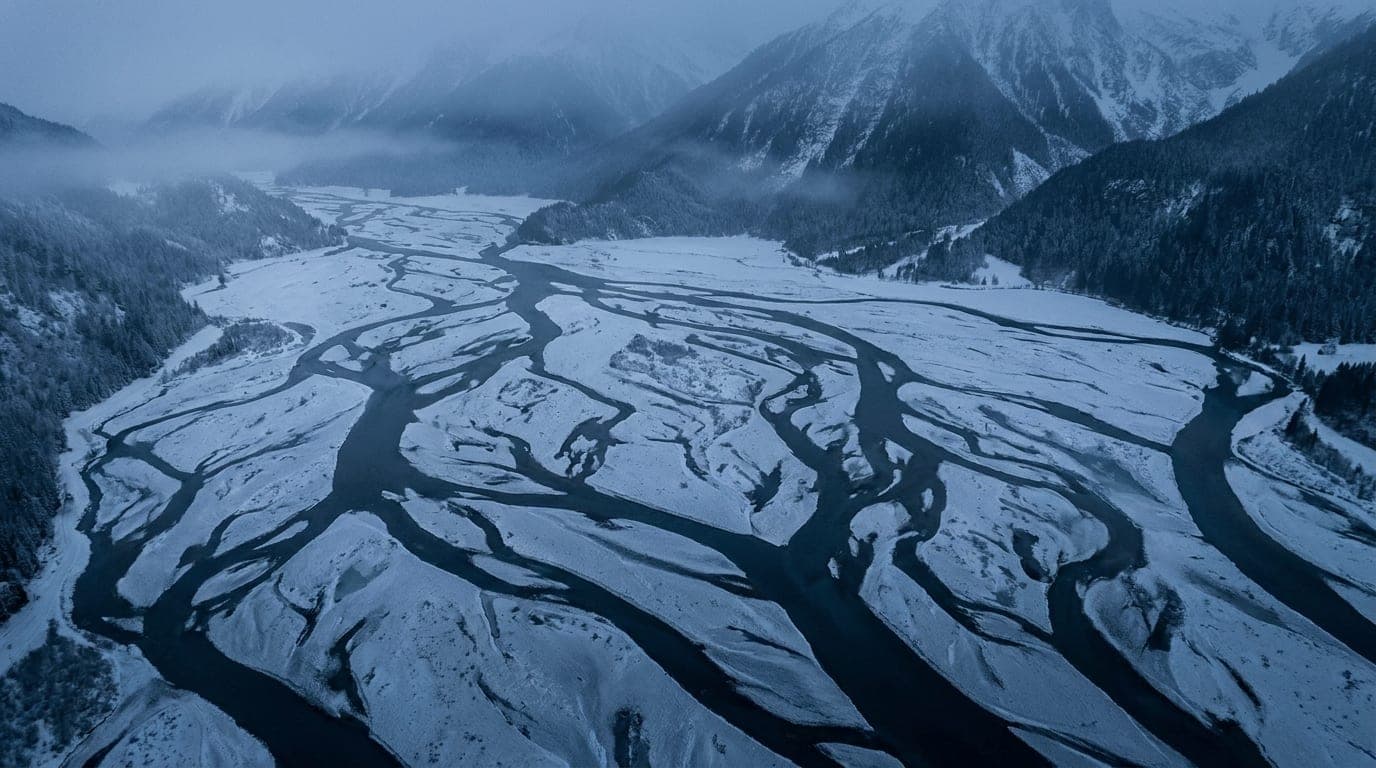 Kühle Alpenlandschaft in Blaustunden-Tönen: ineinandergreifende Flussarme, die aus der Vogelperspektive ein feines Netz bilden.