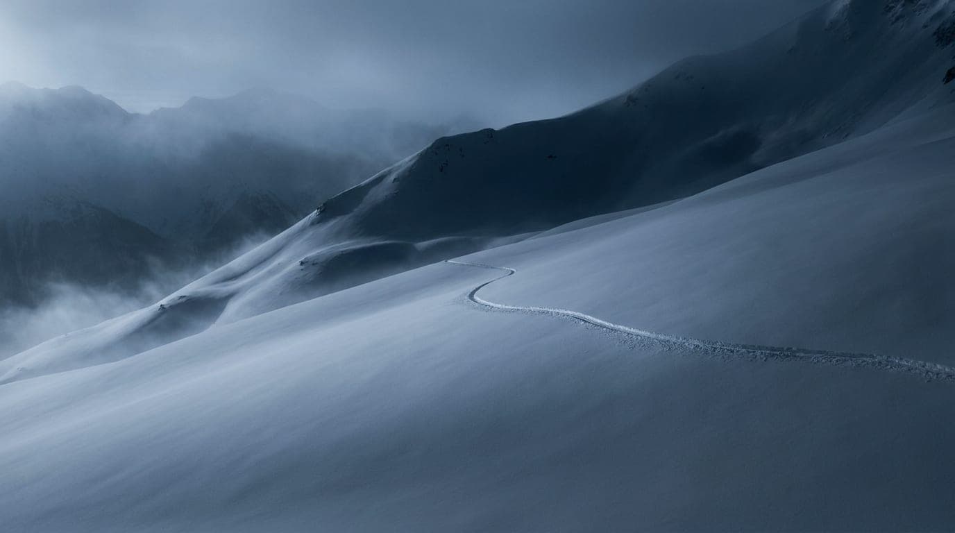 Kühle Alpenlandschaft in Blaustunden-Tönen: eine einzelne klare Spur, die einen glatten Schneehang quert.